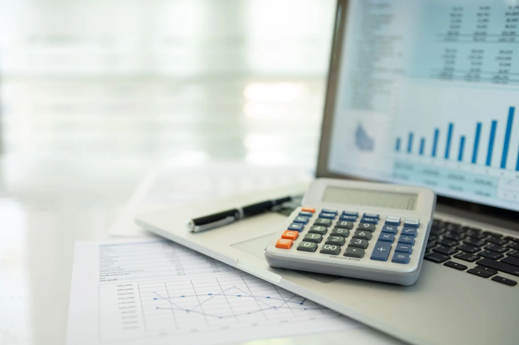Calculator, laptop, and financial documents on desk.