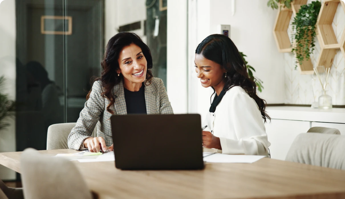 Two women smiling and working on laptop.