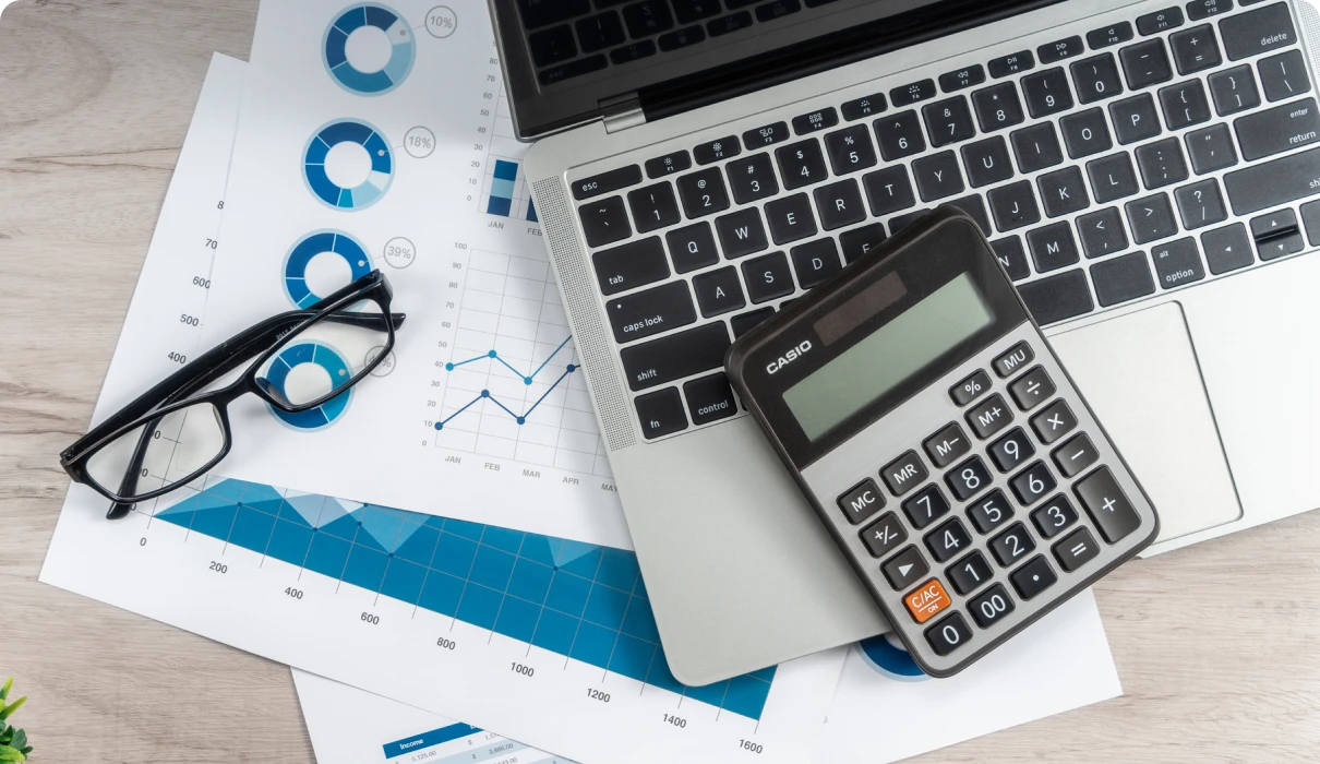 Calculator, laptop, glasses, and charts on desk.