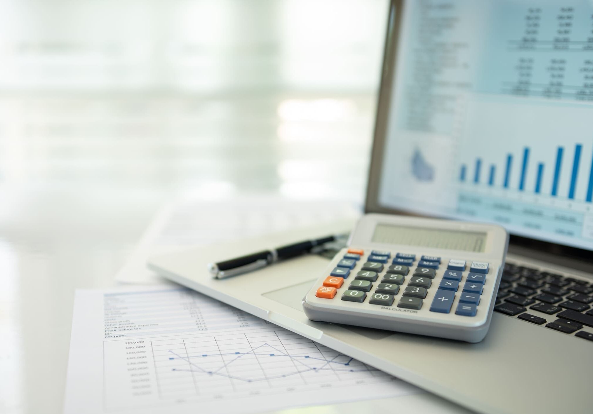 Calculator, laptop, and financial documents on desk.
